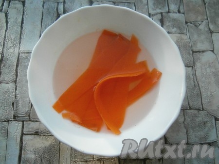 Морковь очистить, срезать овощечисткой штук 6 тонких слайсов, которые залить кипятком и оставить минут на 10 (слайсы станут украшением салата "Подарок"). Оставшаяся морковь в дальнейшем станет одним из слоёв салата.
