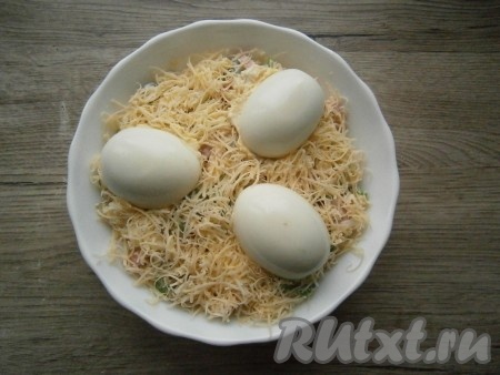 Выложить салат в подходящий салатник, разровнять, посыпать натертым на мелкой терке сыром. Разместить сверху фаршированные половинки яиц желтковой смесью вниз. 