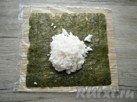 На циновке, обернутой пленкой, расположить лист нори шершавой стороной кверху, выложить рис. 