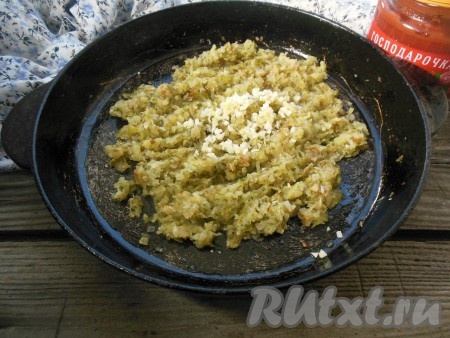 Добавьте измельченный чеснок в сковороду к соленым огурцам, тушеным с луком. 