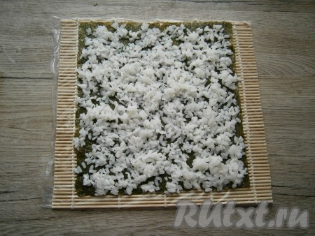Лист нори разложить на циновке шершавой стороной кверху. Тонким слоем распределить по всему листу отваренный рис для суши и роллов.
