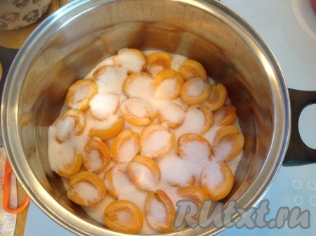 Разделить абрикосы на половинки и вытащить косточки. Уложить половинки абрикосов рядами в кастрюлю, пересыпая сахаром.
