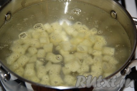 В кастрюлю влить 2,3-2,5 литра воды. Довести воду до кипения. Картофель очистить, нарезать на кубики, выложить в кастрюлю с кипящей водой, снова дать закипеть.
