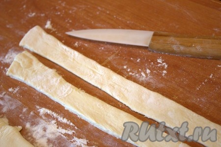 Разморозить слоёное тесто при комнатной температуре. "Припылить" мукой рабочую поверхность, выложить размороженное слоёное тесто и раскатать его в одном направлении, нарезать на длинные, узкие полоски шириной 1,5-2 сантиметра.
