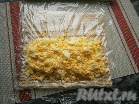 На циновку поместить лист пищевой плёнки. Выложить на одну сторону плёнки белково-желтковую массу.
