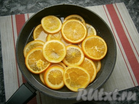 Нагреть сироп и проварить его на небольшом огне, помешивая, до растворения сахара. После этого поместить в сироп кружочки апельсинов.
