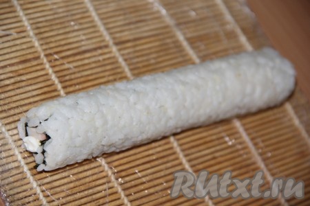 С помощью циновки завернуть плотный ролл. Заворачиваем, начиная со стороны с рисом, а пустая полоска листа нори закрепляет ролл.
