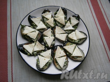 На каждый кружочек баклажана, поверх соуса, выложить по 2 треугольничка сыра.

