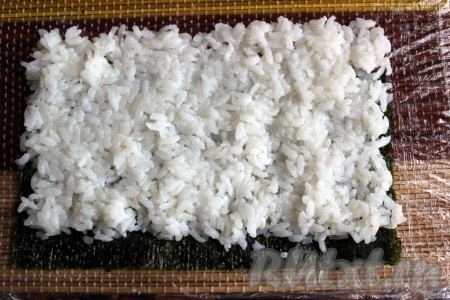 На нори выложить тонкий слой риса следующим образом - с одной стороны оставив 1,5 см нори без риса, а с другой стороны, так сказать, выехать рисом тоже на 1,5 см.