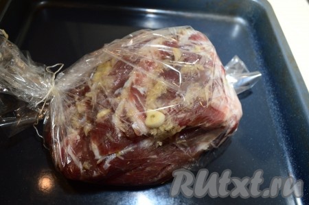 По прошествии времени выложите мясо с чесноком в рукав для запекания. Тщательно завяжите рукав с мясом с двух сторон. Отправьте свинину запекаться в разогретую до 190-200 градусов духовку на 1 час.
