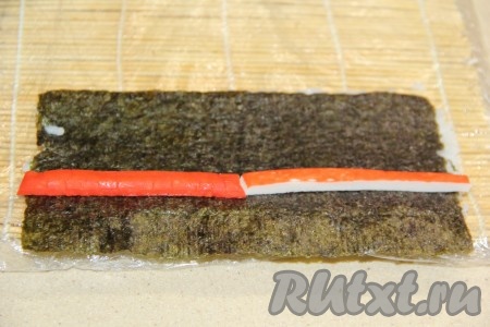 Перевернуть лист нори рисом вниз. Выложить брусочки крабовых палочек.
