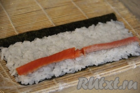 Выложить на рис ближе к широкому краю с рисом брусочки рыбы.