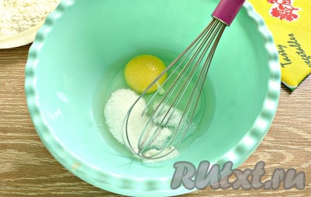 В отдельную миску разбить сырое куриной яйцо, всыпать к нему сахар и соль, взбить венчиком до получения однородной смеси (достаточно будет взбивать в течение 2 минут).