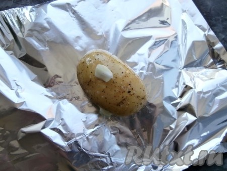 Каждую картофелину поместить на сложенный вдвое лист фольги, сверху выложить по очищенному зубчику чеснока, разрезанного на 2-4 части, а также влить немного растительного масла, которое останется в миске.
