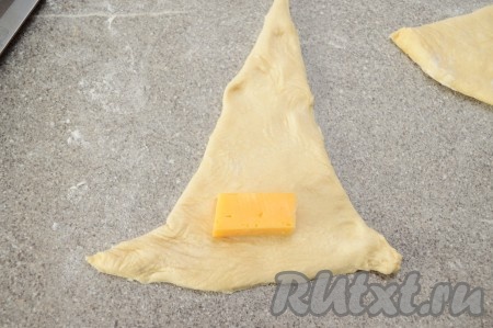 Твёрдый сыр нарезаем на небольшие брусочки. На широкую часть каждого треугольника выкладываем брусочек сыра. Два угла теста, ближайших к сыру, немного растягиваем. Слишком много сыра не стоит класть, иначе он может вытечь во время выпечки.