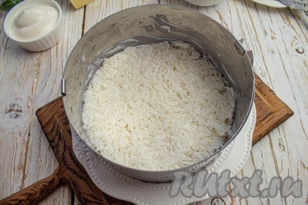 На плоскую тарелку установите кулинарное кольцо (у меня кольцо диаметром 16 см). Первым слоем выложите рис с майонезом. Можете отдельно перемешать майонез с рисом и приправить по вкусу или смазать рис уже в форме.