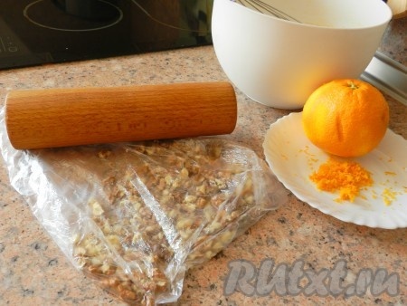 Апельсин тщательно вымыть и снять с него цедру. Орехи очистить, сложить в пакет и прокатать скалкой, чтобы немного их измельчить, но не в крошку.