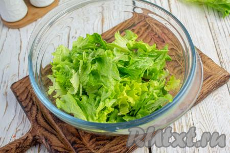 Промойте и обсушите листья салата, затем порвите их руками на небольшие кусочки и сложите в салатник.