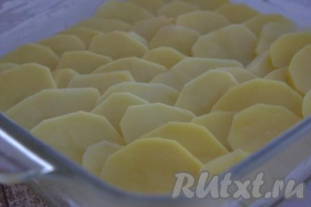 Форму для запекания смазать тонким слоем сливочного масла. Выложить внахлёст половину нарезанного картофеля.