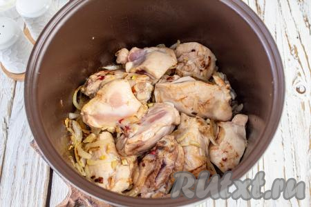 Кусочки курицы выложите в чашу мультиварки к луку с чесноком и готовьте с одной стороны 10 минут, затем переверните и обжаривайте ещё 7-8 минут. Когда курочка немного обжарится, слегка приправьте её солью и молотым перцем.