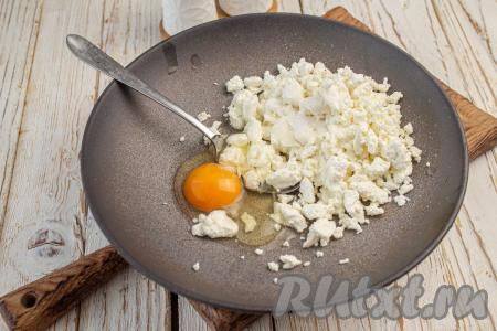 В миску выложите творог, вбейте куриное яйцо и добавьте соль по вкусу, хорошо перемешайте столовой ложкой (или вилкой).
