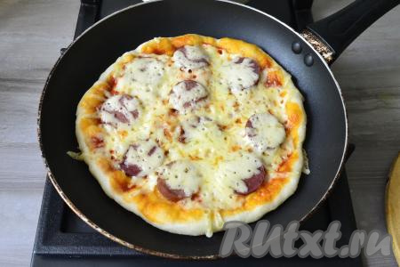 Накрыть сковороду крышкой и готовить дрожжевую пиццу на минимальном огне 10 минут. Затем переложить на тарелку. Аналогично испечь вторую пиццу. 