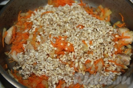 Немного потомив морковку, снимаем сковороду с огня и добавляем к зажарке перловку. 