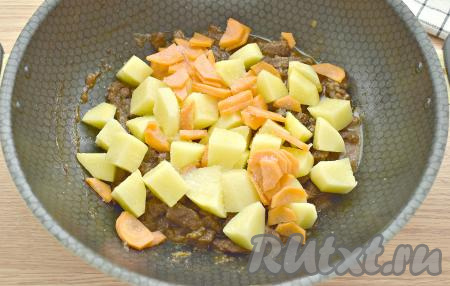 Картошку очищаем. Когда говядина станет мягкой, добавляем в сковороду картошку, нарезанную на крупные кубики, и нарезанную полукружочками морковку, солим, перемешиваем, продолжаем готовить дальше ещё 10 минут, помешивая время от времени. 