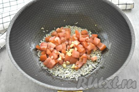 К луку добавляем нарезанный на кусочки помидор и мелко порубленные зубчики чеснока, перемешиваем, обжариваем минуты 4, помешивая.