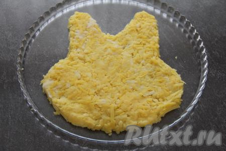На плоскую тарелку выложить натёртый на крупной тёрке отварной картофель в виде мордочки кролика, посолить.