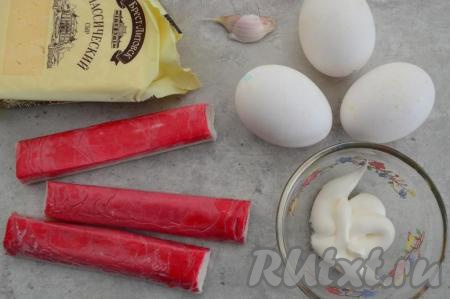 Подготовить продукты для приготовления яиц, фаршированных крабовыми палочками, сыром и чесноком. Отварить яйца в течение 10 минут после закипания воды, после этого залить их очень холодной водой и оставить остывать. После остывания очистить. Крабовые палочки заранее достать из морозилки, чтобы они слегка разморозились (полностью размораживать их не нужно, тогда они легче будут в дальнейшем натираться на тёрке). Для приготовления этой закуски подойдёт любой сыр твёрдых сортов. Чеснок очистить.