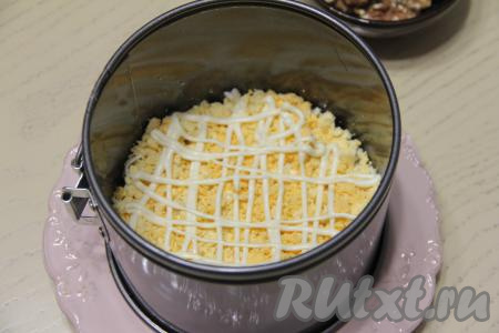 Яйца почистить, разделить на белки и желтки. Раскрошить желтки и выложить равномерно поверх сыра. Нанести решётку из майонеза и слегка утрамбовать слои.