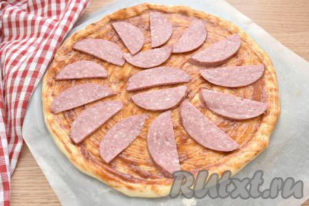 На смазанную основу пиццы выкладываем копчёную колбасу, нарезанную на достаточно тонкие полукружочки.