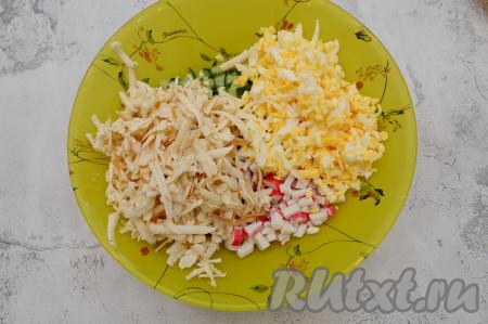 Яйца и колбасный сыр натереть на крупной тёрке и переложить к крабовым палочкам и огурцам.