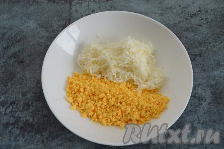В отдельной тарелке вилкой растираем желтки в крошку. Натираем на мелкой тёрке сыр и добавляем его к желткам.