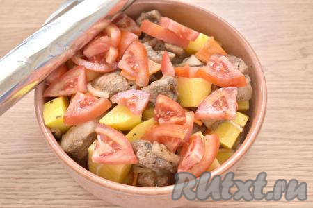 Поверх свинины с картошкой и овощами, по желанию, раскладываем помидор, нарезанный на ломтики. Форму накрываем фольгой и отправляем в разогретую до 190 градусов духовку.