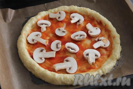 Основу картофельной пиццы смазать томатным соусом. Шампиньоны промыть и тонко нарезать, выложить грибы на основу.