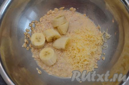 Сыр натереть на средней тёрке. В миску с овсяной массой выложить ту половину банана, которая нарезана на крупные кусочки, сюда же добавить половину натёртого сыра.
