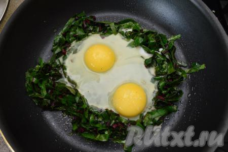 В центр кольца вбить сырые яйца, посолить их, можно немного поперчить. Сделать огонь ниже среднего. Жарить яичницу со свекольной ботвой минуты 3-4. Я люблю, чтобы белок хорошо схватился, а желтки были ещё жидкими внутри, поэтому сковороду крышкой не накрываю. Если вы предпочитаете, чтобы желтки "схватились", тогда сразу сковороду с яйцами накройте крышкой.