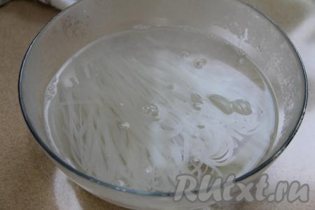 Пока обжаривается морковь, в глубокую миску выложить рисовую лапшу, залить её большим количеством кипящей воды и оставить на 3-4 минуты. Затем откинуть лапшу на дуршлаг, промыть холодной водой, дать стечь лишней воде.