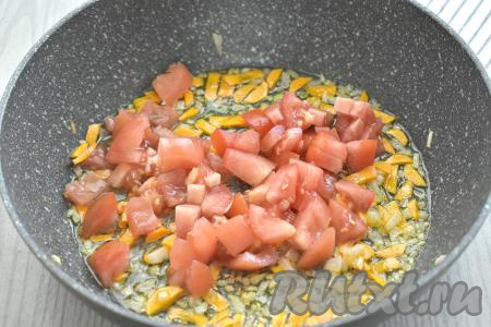 С помидоров, по желанию, снимаем кожуру, нарезаем на небольшие кубики, выкладываем к обжаренным овощам, перемешиваем и готовим 2-3 минуты, не забывая иногда помешивать.