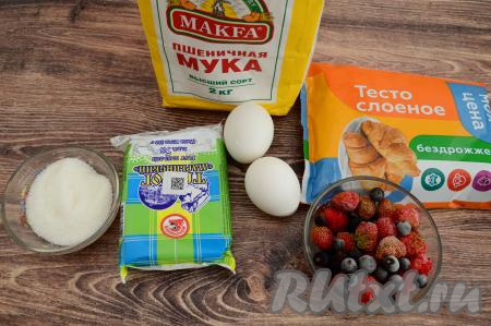 Подготовить продукты для приготовления пирога с творогом и ягодами из слоёного теста. Слоёное тесто для этого открытого пирога можно взять как дрожжевое, так и бездрожжевое. Я взяла бездрожжевое. Тесто разморозить при комнатной температуре. Ягоды можно взять как свежие, так и замороженные. Я взяла замороженную клубнику и чёрную смородину. Замороженные ягоды можно не размораживать, если на них нет большого количества наледи. Свежие ягоды нужно будет промыть, обсушить, разложив их на бумажном полотенце. Если у ягод крупные косточки (например, у вишни), тогда косточки обязательно нужно будет удалить.