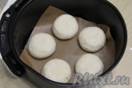 На отдельную тарелку насыпать 2 столовых ложки рисовой муки. Руками, смоченный водой, из каждой части творожной массы сформировать округлый сырник, затем обвалять его со всех сторон в рисовой муке. Дно чаши для аэрогриля застелить пергаментом, выложить сформированные сырники.