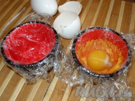 Чашки выстелить пищевой плёнкой, чтобы концы плёнки свисали за пределы чашки. Яйцо аккуратно разбить и вылить в чашку так, чтобы желток обязательно остался целым.
