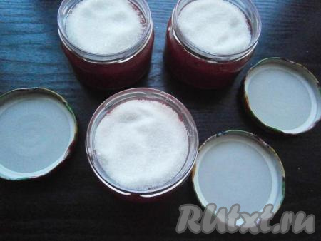 Сверху каждой баночки всыпать по 2 столовые ложки сахара, покрыв им малину (как на фото).