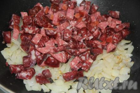 Колбасу (или колбаски) нарезать на средние кусочки и добавить в сковороду к луку, перемешать и обжарить пару минут.