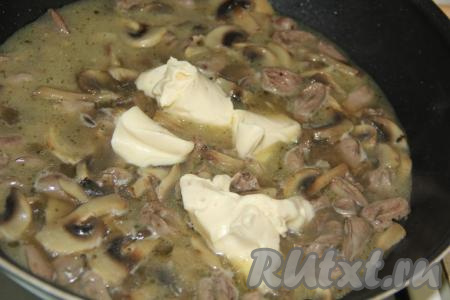 Добавить плавленный сыр в сковороду к куриным сердечкам и шампиньонам. Перемешивать блюдо до полного расплавления сыра.