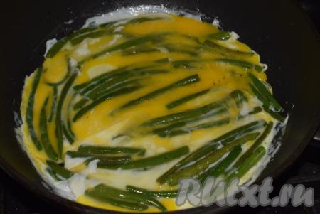 К обжаренной стручковой фасоли вбиваем яйца и распределяем их по всему периметру сковороды, накрываем крышкой и даем блюду протомиться на среднем огне около 3-4 минут (до готовности яиц).