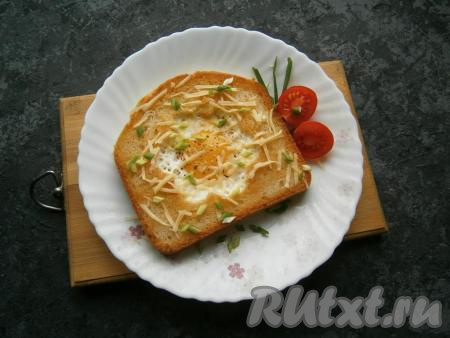 Яичницу, приготовленную в хлебе, переложить со сковороды на тарелку, посолить и поперчить, посыпать натертым сыром и измельченным зеленым лучком. 