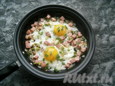 Сковороду прикрыть крышкой и жарить яичницу с колбасой и луком на небольшом огне до тех пор, пока яичный белок полностью не свернется, а желток останется жидким (минуты 3-4). Яйца посолить и поперчить, посыпать измельченным зеленым луком.